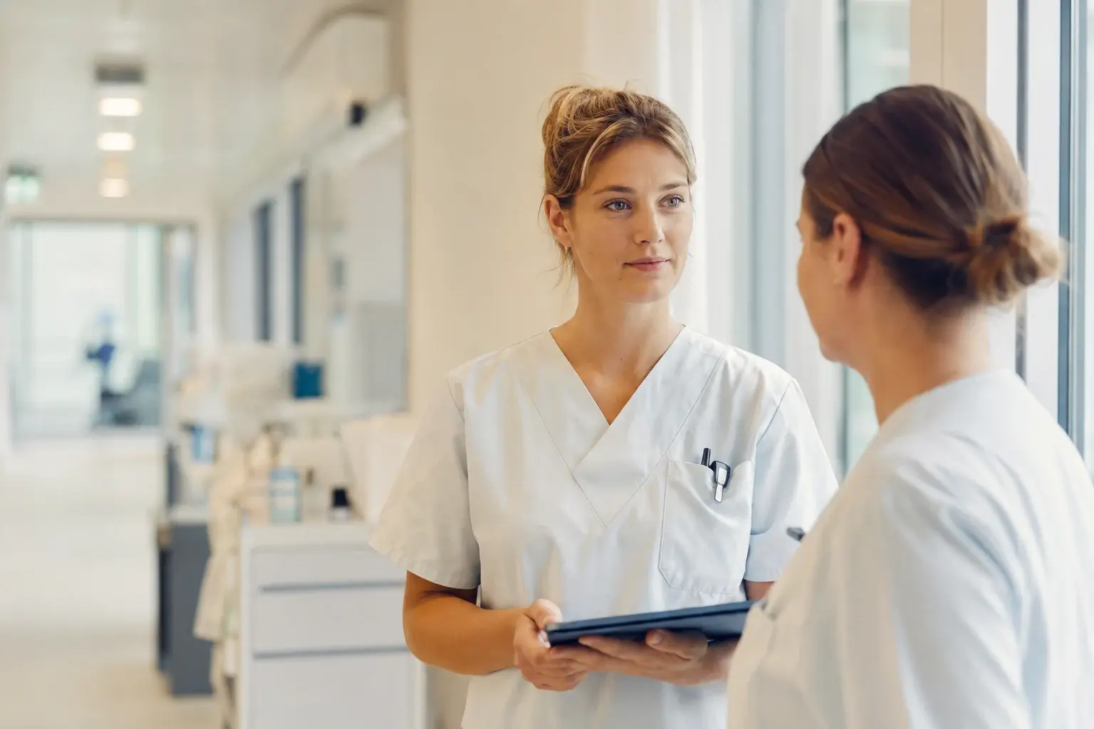 Pflegefachkräfte führen eine ruhige Übergabe im Klinik- oder Pflegeumfeld.